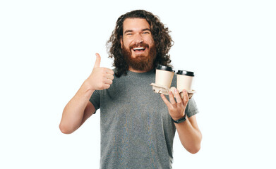 Charming handsome bearded man showing thumb up and holding two cups of coffee on the go