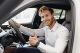 Fototapeta  - Man customer buyer businessman client in classic suit sit in car salon show thumb up chooses auto wants to buy new automobile in showroom vehicle dealership store motor show indoor Car sales concept