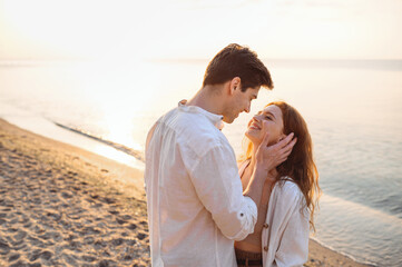 Wall Mural - Side view tender young couple two friend family man woman in white clothes boyfriend hug girlfriend hold face going to kiss at sunrise over sea beach ocean outside seaside in summer day sunset evening