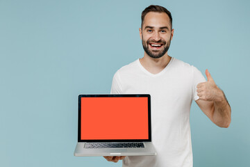 Wall Mural - Young smiling man in white blank print design t-shirt hold use work on laptop pc computer with blank screen workspace area show thumb up gesture isolated on plain pastel light blue background studio.