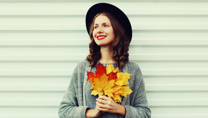 autumn portrait of happy smiling young woman with yellow maple leaves looking away wearing a black r