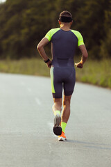 Wall Mural - Young professional male triathlete, runner in motion on open road. Concept of sport, lifestyle, activity. Back view