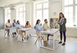 © Studio Romantic - Experienced female business coach explains the strategy of a marketing seminar to adult students. Woman teaches a variety of adult women and men sitting at desks in a modern business school classroom.