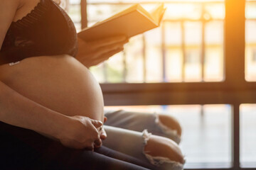 A pregnant woman and a young man in love sit by the window in the morning reading the Bible to learn God's teachings from the Bible with belief and faith and pray for the safety of the unborn child.