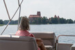 Trakai Lithuania - July 12 2021: Blonde woman in pink blouse sitting on beige gray leather seats of a touristic boat and looking towards medieval fortress on a island.