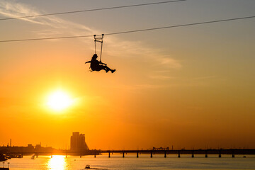 Wall Mural - Silhouette of young woman riding zipline over the river Dnieper. Dnipro, Ukraine
