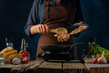 The cook fries chicken fillets in a pan for Caesar salad. Salad ingredients. Dark background. Wooden table. Close-up. Careful viewing.