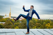 Emotional happy stylish young man stands on the roof of the building on one leg. Joyful emotions and a smile. Against the background of the sights of the city of St. Petersburg, Russia.