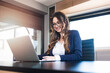© Bojan Topalovic - Beautiful lady with long hair and glasses sitting in modern office, working on laptop and smiling.