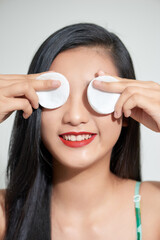 Wall Mural - Pretty beauty young Asian woman covering her eyes with cotton pad over white isolated background. Healthy skin and cosmetics concept.