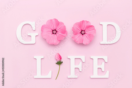 Good life. Motivational quote from white letters and beauty natural flowers on pink background. Creative concept inspirational quote of the day