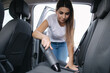 © Aleksandr - Woman vacuuming backseat in her car in the garage at home. Female using portable vacuum cleaner to remove dust and dirt. Car interior cleaning