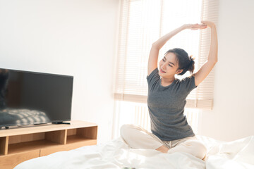 Wall Mural - Bedroom concept in the morning the pretty girl just waking up and stretching her body on the brown wooden bed