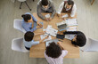 Team of people having important discussion in business meeting. Group of men and women working with sales reports sitting around wooden table in modern office, high angle, view from above, top view
