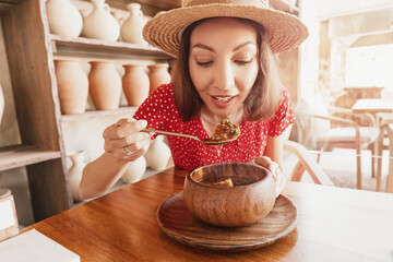 Wall Mural - Happy woman eats kharcho soup from Georgian cuisine or Hungarian meat goulash in a rustic restaurant.