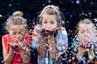 Young girls having fun celebrating while blowing confetti at party outdoor - Focus on center hands kid