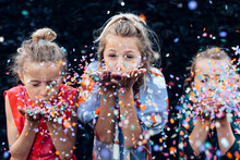 Young Girls Having Fun Celebrating While Blowing Confetti At Party Outdoor - Focus On Center Hands Kid