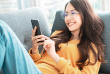 Happy Asian Woman Using Mobile Phone. Smiling Young Female Using App Shopping Online, Ordering Delivery Relax On Sofa At Home.