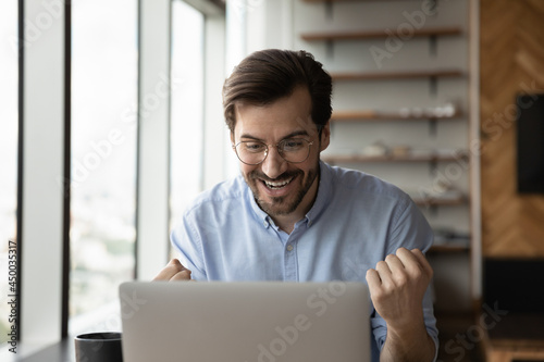 Happy excited laptop user getting amazing good news, looking at screen, making yes winner gesture, celebrating job result, work achieve, success, reward. Surprised overjoyed employee getting promotion