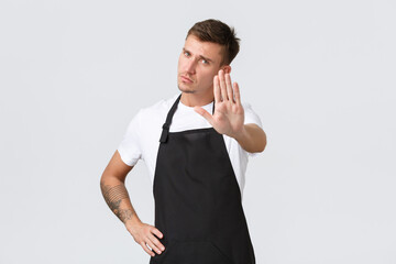 Employees, grocery stores and coffee shop concept. Serious-looking displeased barista, waiter in black apron extend hand for stop gesture, prohibit entering cafe, forbid action, white background