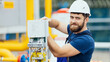 © SerPak - Electrician in a helmet and overalls works adjusts the equipment looks into the camera and smiles. A positive portrait of a kind Caucasian worker with a beard at work. Energy Industry Service