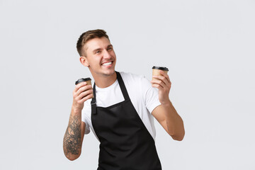 Wall Mural - Small business, coffee shop, cafe and restaurants concept. Enthusiastic happy barista in black apron holding two paper cups with coffee, selling and giving order to clients, laughing joyfully