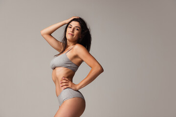 portrait of young beautiful slim woman in lingerie posing isolated over gray studio background. natu