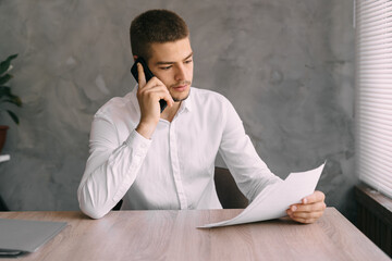 business people and communication concept young man talking on mobile phone while working with documents in home office. Workplace businessman making a call communicating with a client.