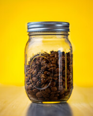 Poster - Closeup shot of a glass jar with coffee beans on a yellow background