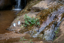 Selective Focus White Sandals Placed On A Rock Beside A Small Waterfall Natural Water Source Near The Village