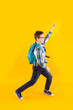 Jumping emotional schoolboy on the yellow background
