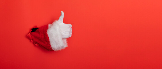 Wall Mural - Santa Claus hand thumbs up through a hole in red paper background