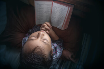 Wall Mural - Top down view little girl praying on the bed with bible in home. Christian prayer concept.