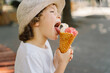 Boy in a hat is holding an ice cream and looks happy and surprised. Summer food and summer time