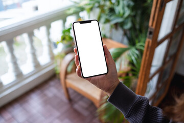 mockup image of a woman holding mobile phone with blank desktop screen on balcony at home
