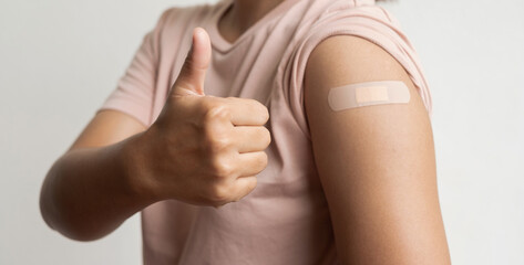 Asian woman shows plaster on her shoulder after being vaccinated against Covid-19. Coronavirus vaccination campaign concept