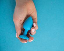 A Woman Is Holding A Blue Anal Plug On A Blue Background. Adult Toy For Alternative Sex