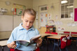 © Austockphoto - Indigenous girl primary school student standing reading a book in a classroom