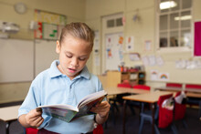 Indigenous Girl Primary School Student Standing Reading A Book In A Classroom