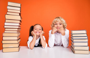 Photo of positive cheerful kids hands cheeks stack book desk wear uniform isolated orange color background