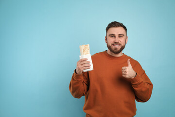 Wall Mural - Young man with delicious shawarma on turquoise background, space for text