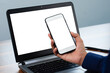 © Suriyo - Hand holding phone mobile phone or smartphone mockup screen with laptop computer on workplace