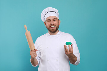 Wall Mural - Happy professional confectioner in uniform with delicious cake and rolling pin on light blue background