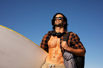 Portrait of handsome surfer with his surfboard. Young man enjoying at the beach