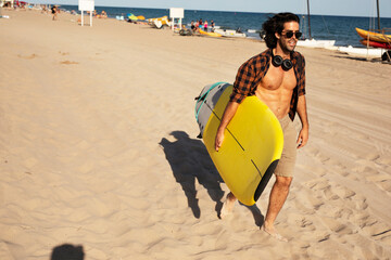 Portrait of handsome surfer with his surfboard. Young man enjoying at the beach