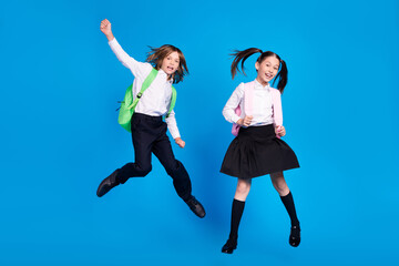 Sticker - Photo of lucky excited schoolkids formalwear backpacks smiling jumping high rising fists isolated blue color background