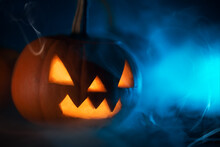 Creepy Halloween Pumpkin Lantern Close-up On A Blue Smoky Background, Copy Space. Holiday Wallpaper Or Postcard