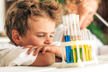 Wall Mural - Serious little boy in white uniform conducts chemical experiments in a laboratory.Back to school concept.Young scientists.Natural sciences.Preschool and school education of children.