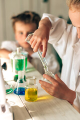 Wall Mural - Serious little boy and girl in white uniforms conducting chemical experiments in a laboratory.Back to school concept.Young scientists.Natural sciences.Preschool and school education of children.