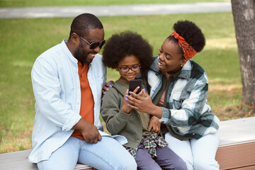 Wall Mural - Happy parents and their son looking at smartphone screen in park